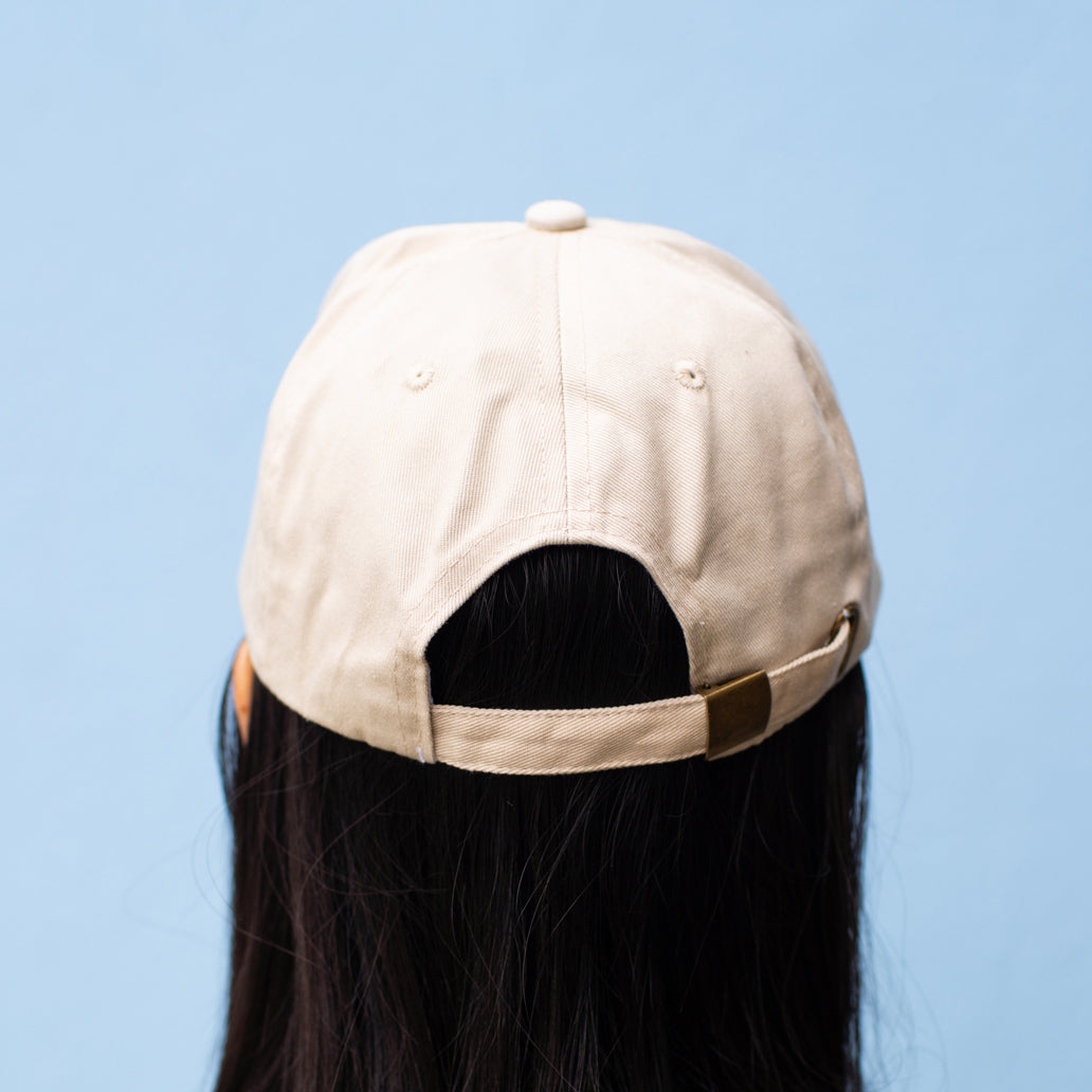 Back of beige baseball cap showing adjustable strap and buckle.