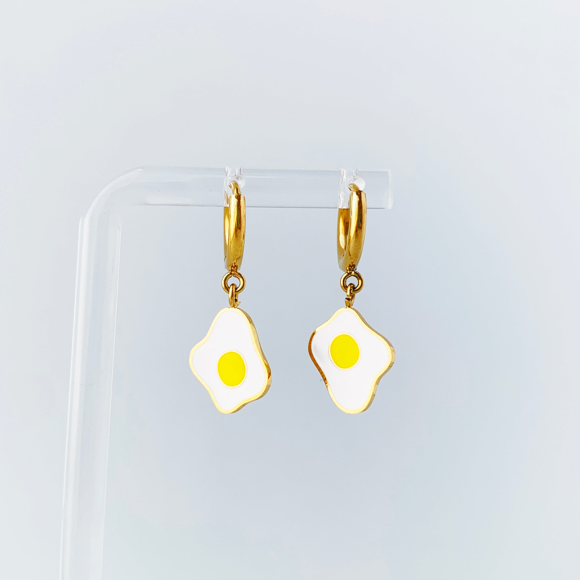 Egg enamel charms on gold huggie hoop earrings hanging on a display