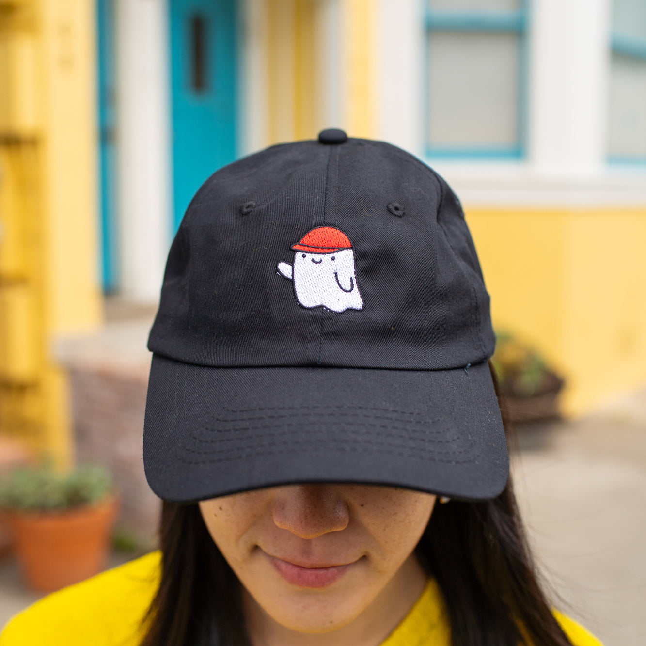 Close up of person wearing black baseball cap with an embroidered ghost wearing a red cap.