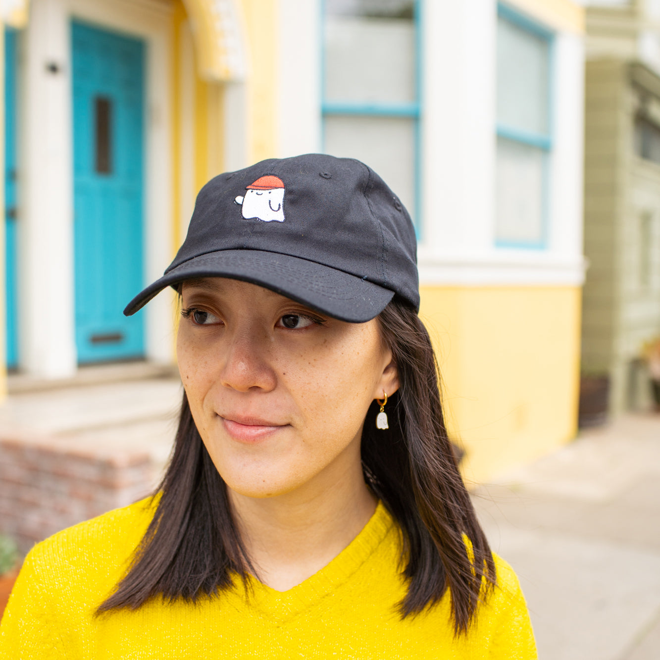Person wearing black baseball cap with an embroidered ghost wearing a red cap.