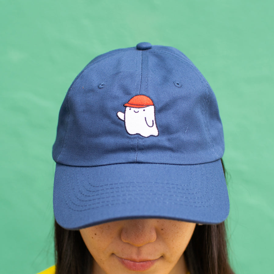 Close up of person wearing navy baseball cap with an embroidered ghost wearing a red cap.