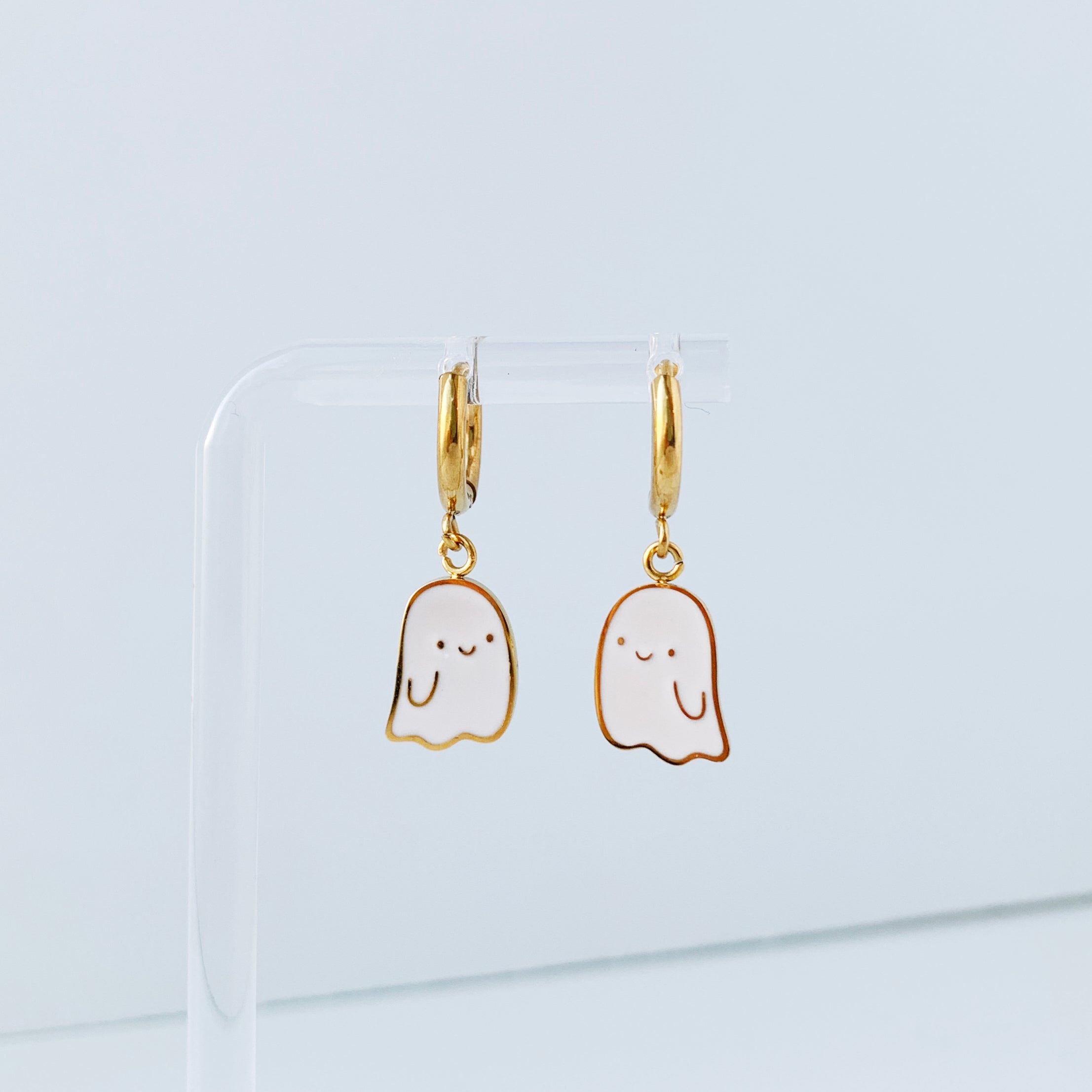 Small gold hoop earrings with charms of a smiling ghost.