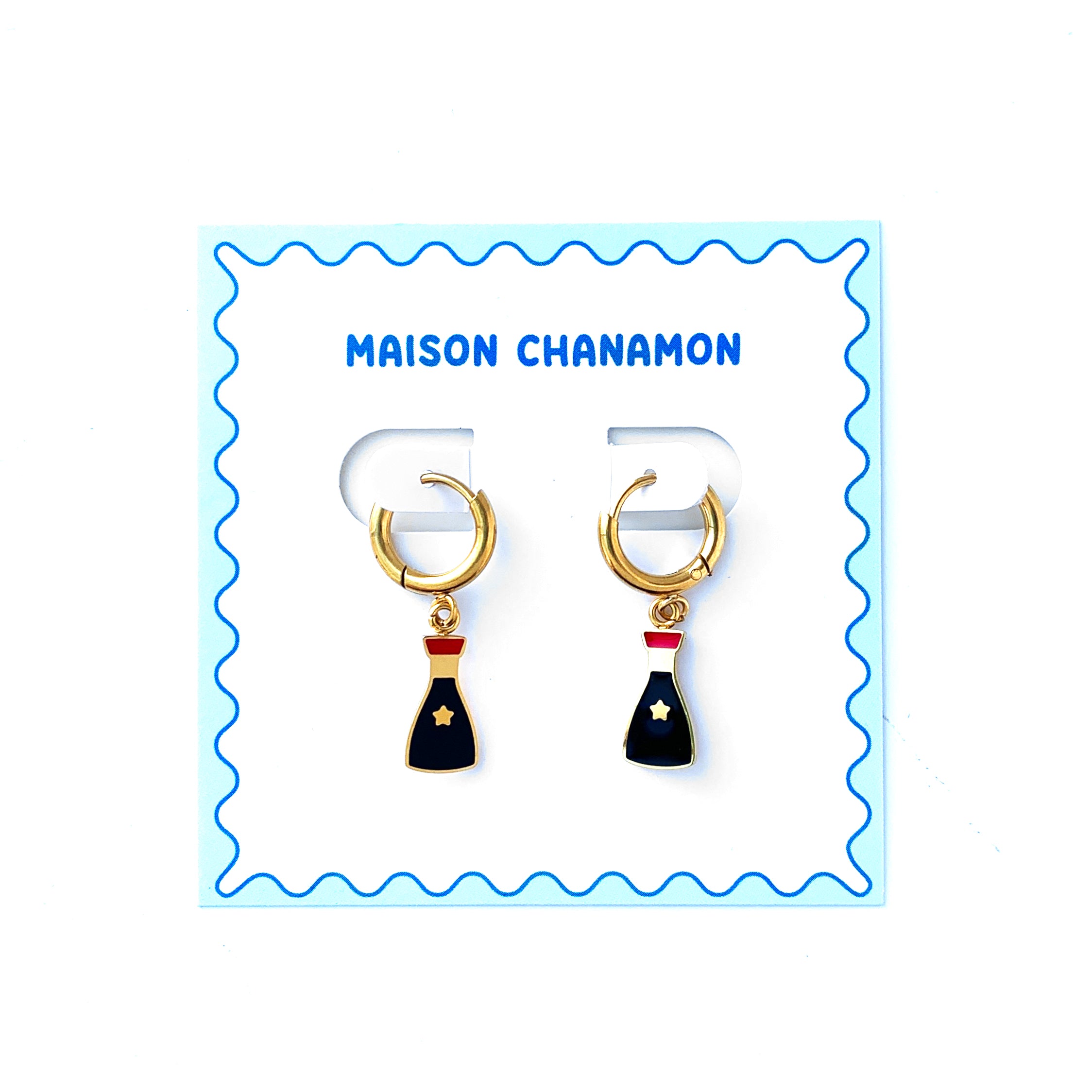 Small gold hoop earrings with charms of a soy sauce bottles on a backing card with a blue squiggle border and "Maison Chanamon" label.
