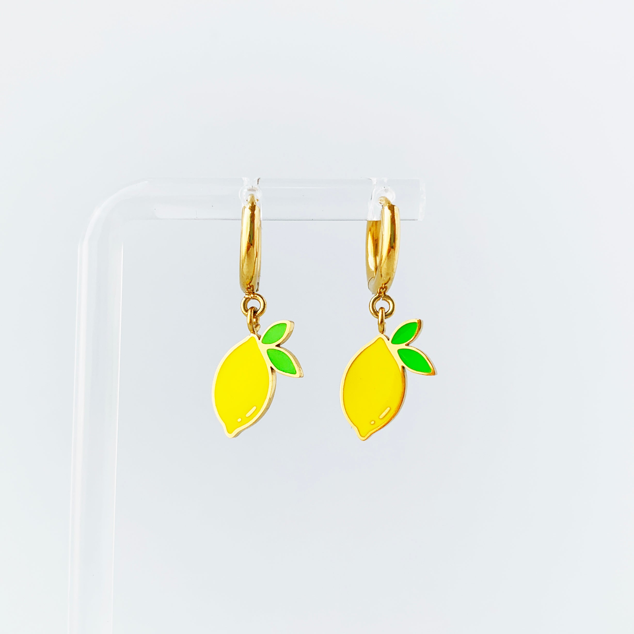 Lemons with 2 leaves enamel charms on gold huggie hoop earrings hanging on a display