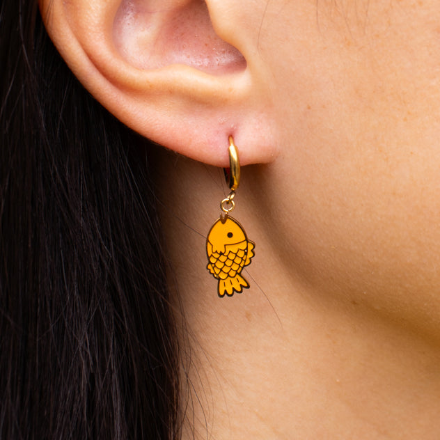 Taiyaki fish charm hanging from a gold huggie hoop, mouth up