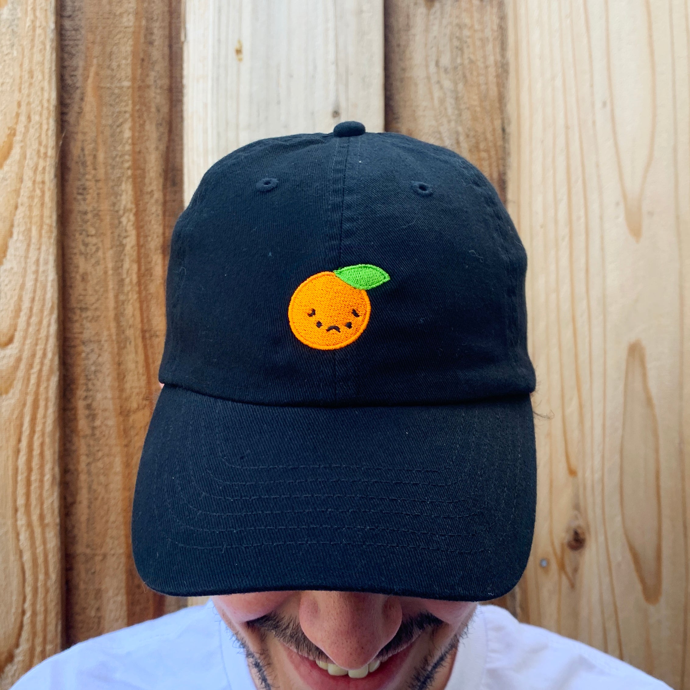 Close up of black baseball cap with sad orange embroidered on front.
