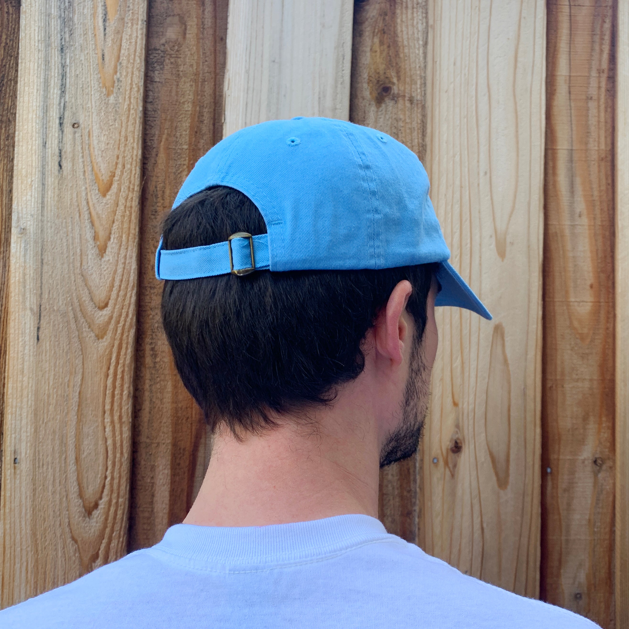 Side angle view of back of sky blue baseball cap with adjustable buckle strap.