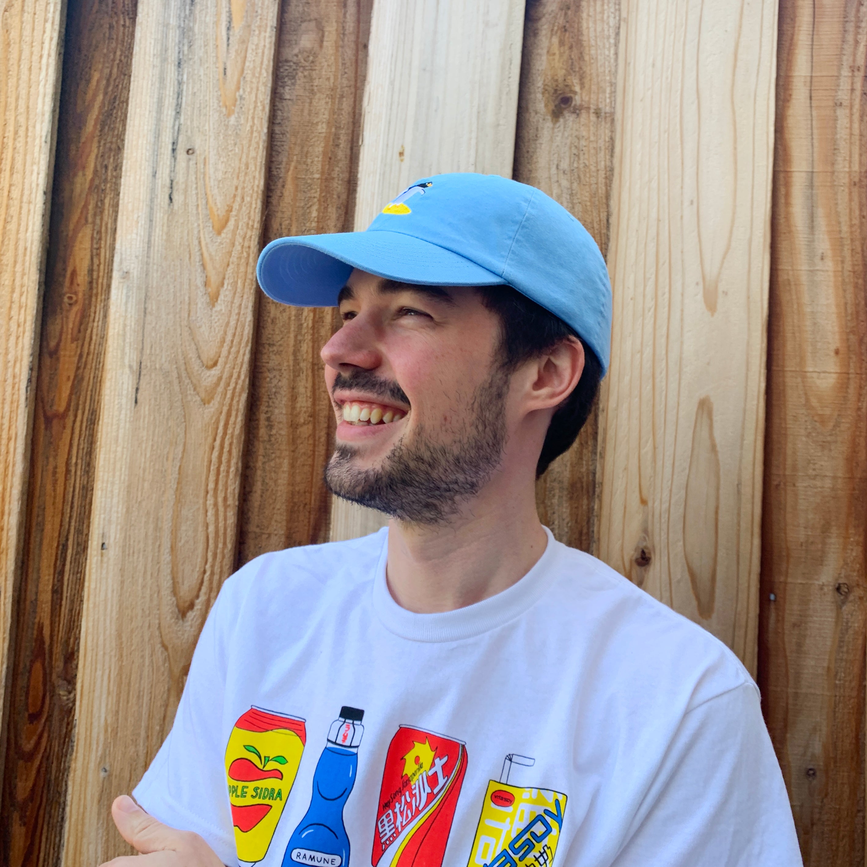 Side angle view of person wearing sky blue baseball cap with a surfing penguin embroidered on the front.