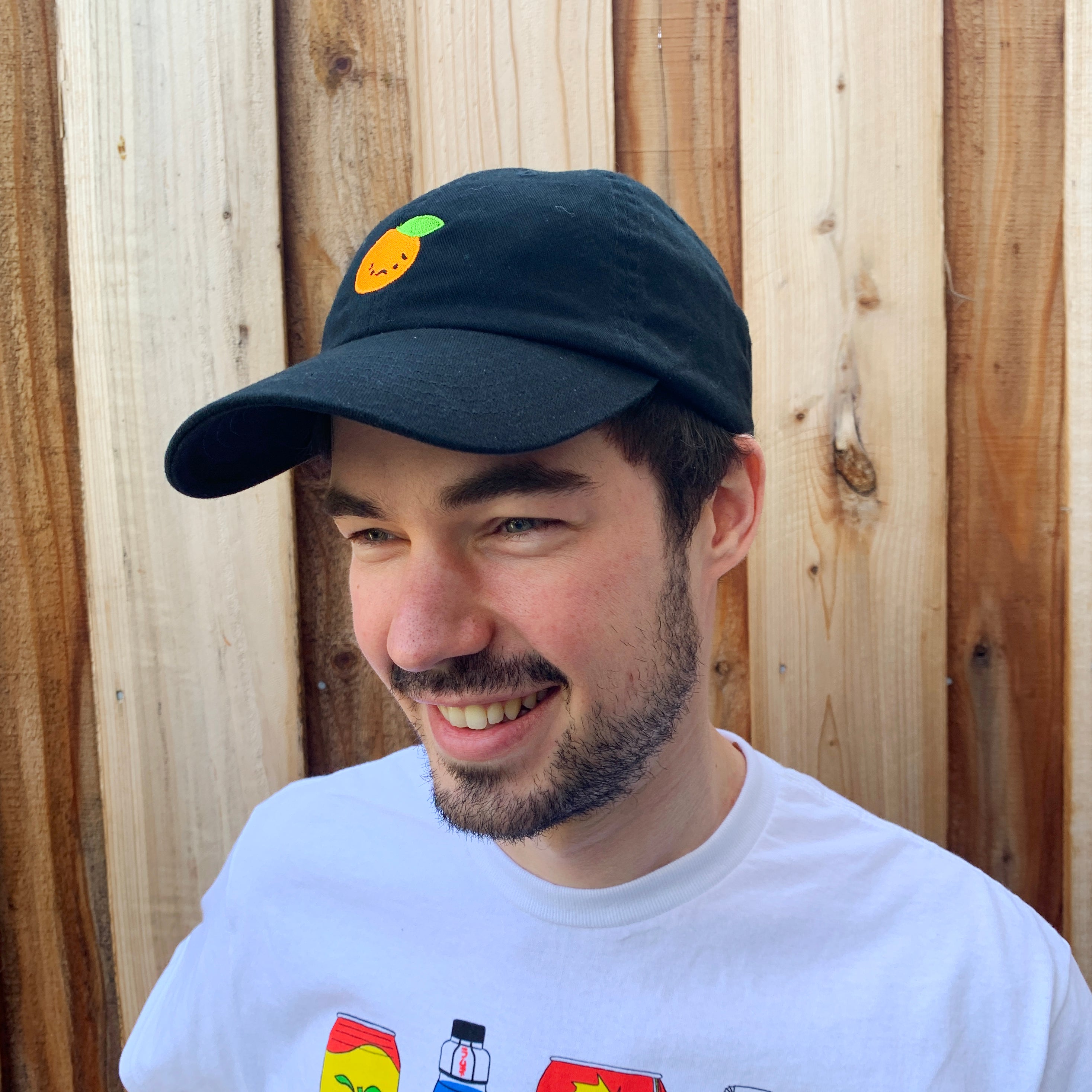 Person smiling wearing black baseball cap with sad orange embroidered on front.