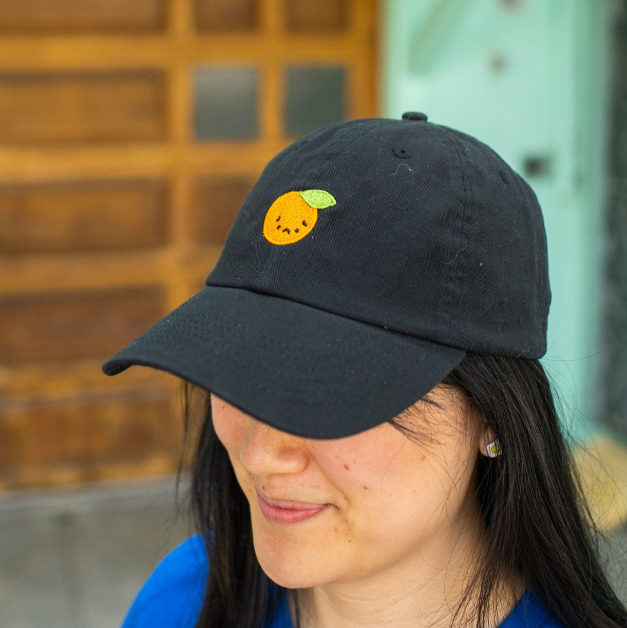 Side angle view of person wearing black baseball cap with sad orange embroidered on front.