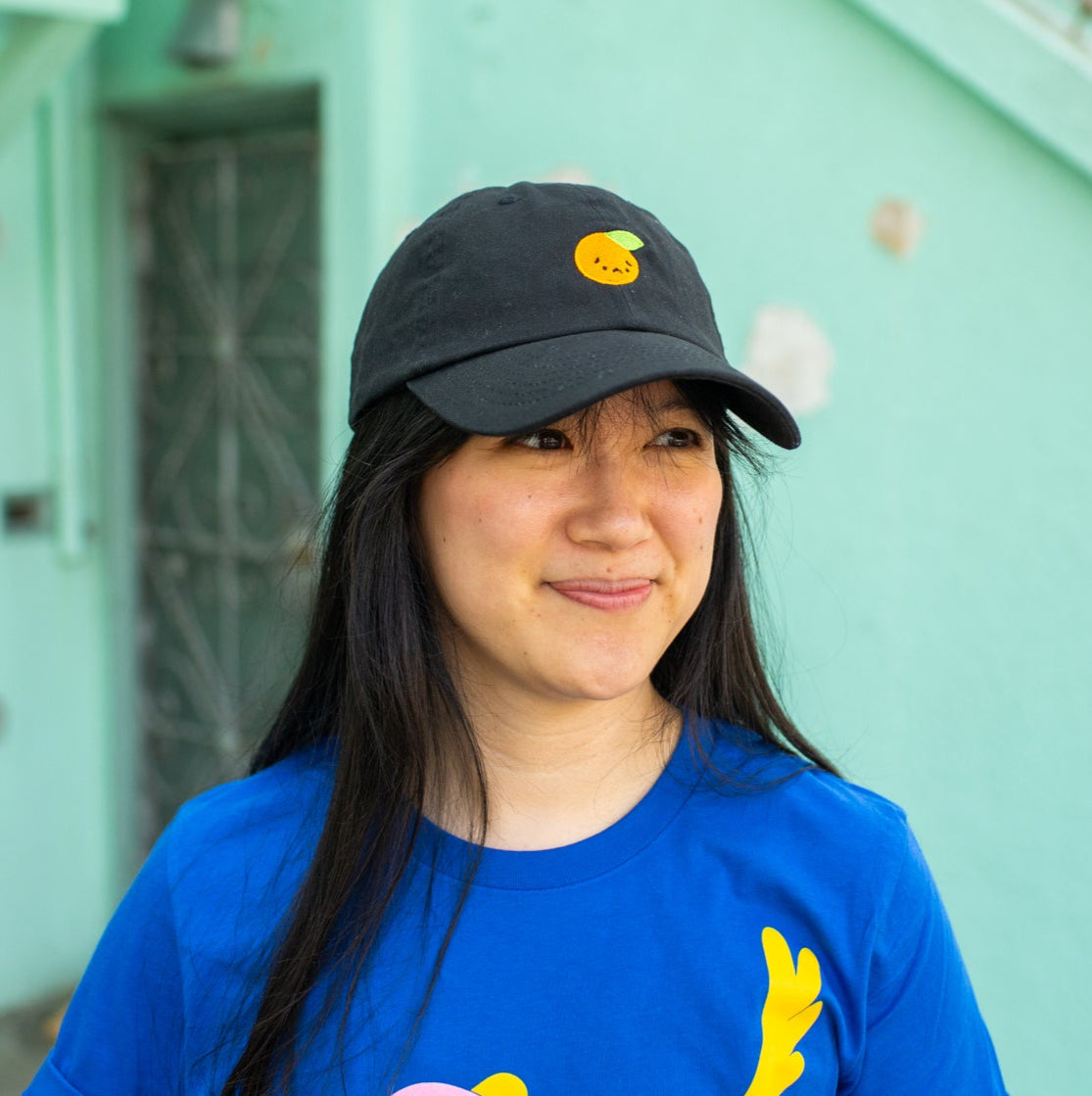 Person smiling wearing black baseball cap with sad orange embroidered on front.